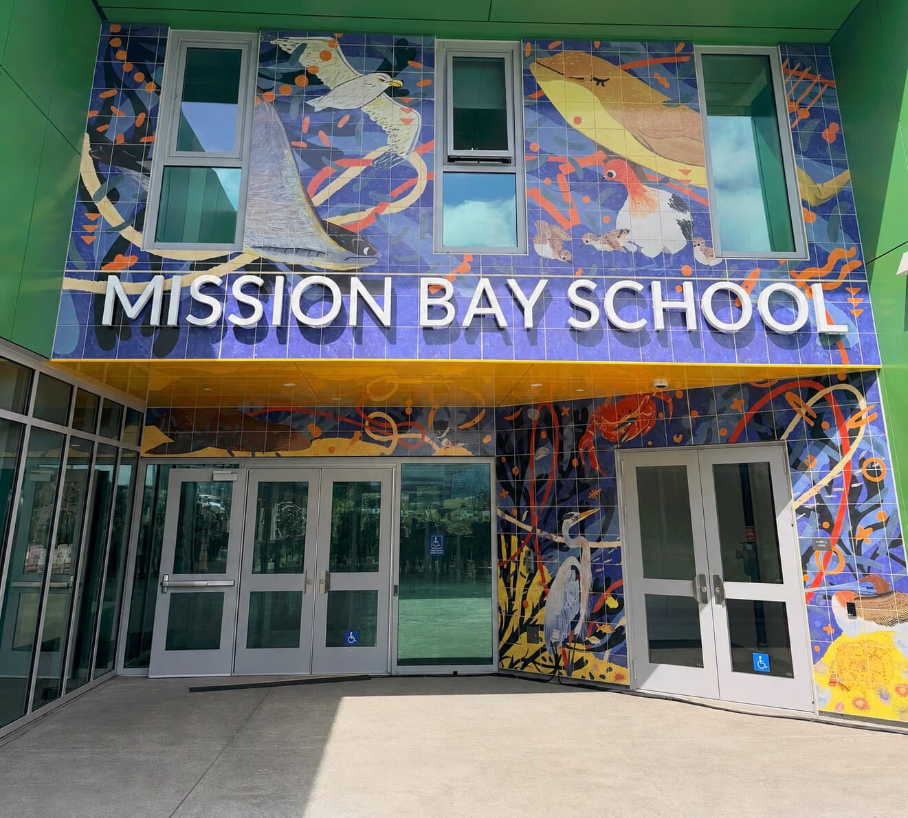 The main entrance on Owens Street: glass doors under a canopy, with the tiled bay-wildlife mural and the school name above them