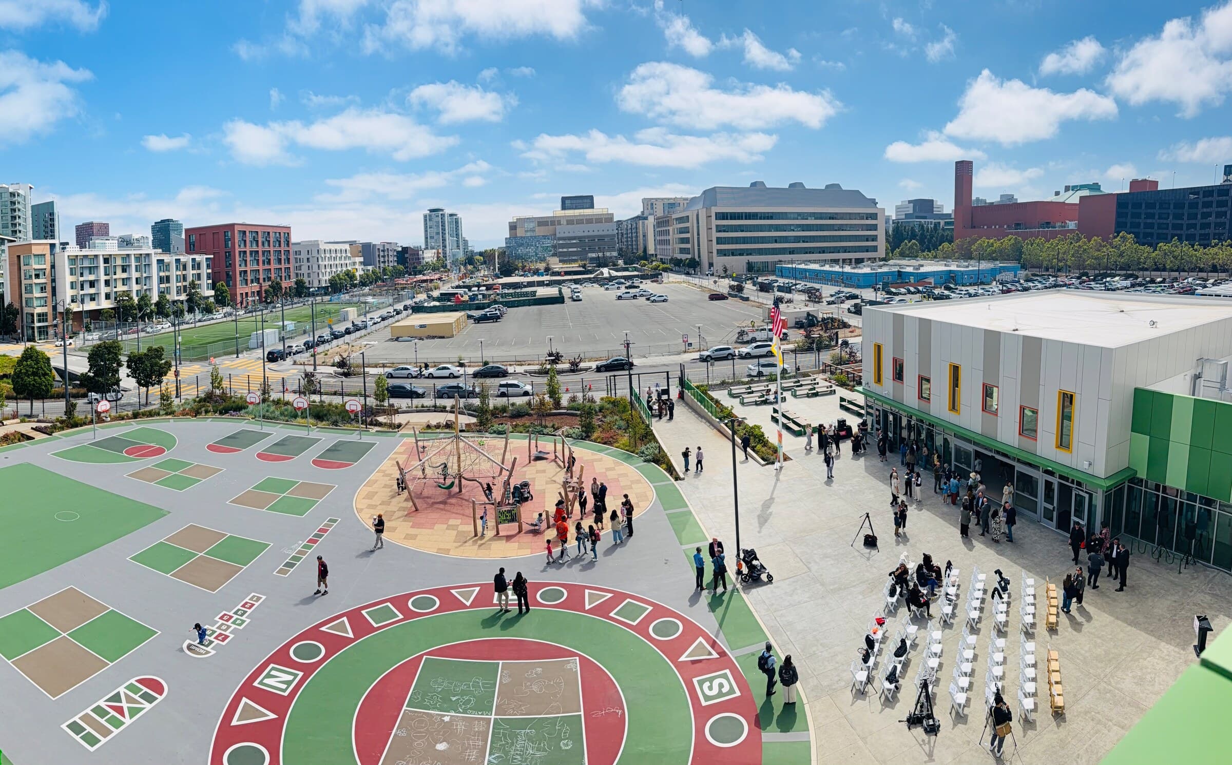The schoolyard from above: painted games, a play structure, and the Mission Bay skyline beyond
